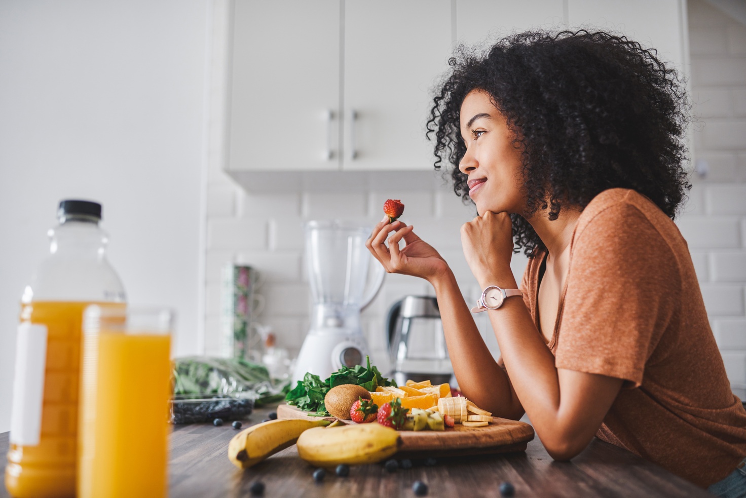 A woman holding a strawberry beside fruit and vegetables in a kitchen